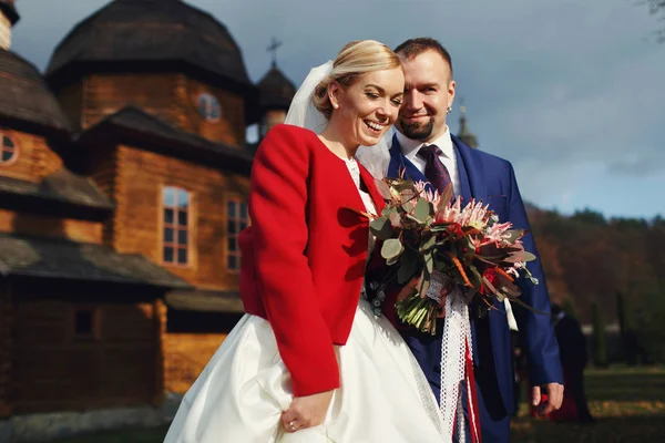 Casal feliz fica na frente de uma igreja de madeira — Fotografia de Stock