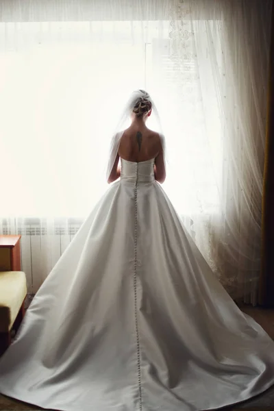 A view from behind on a stunning bride standing at the window — Stock Photo, Image