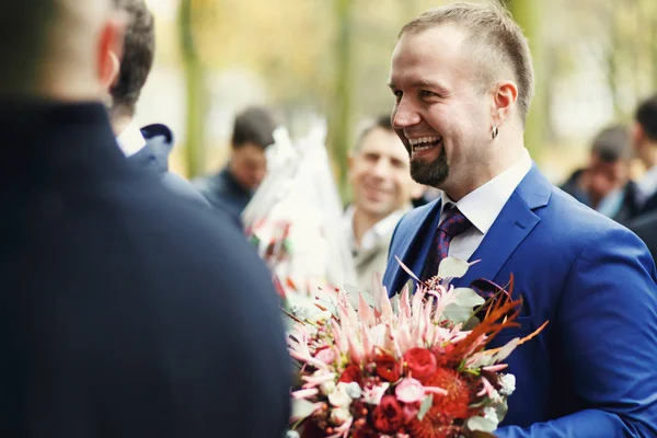 Elegante sposo sorride ampio tenendo un bouquet rosso — Foto Stock