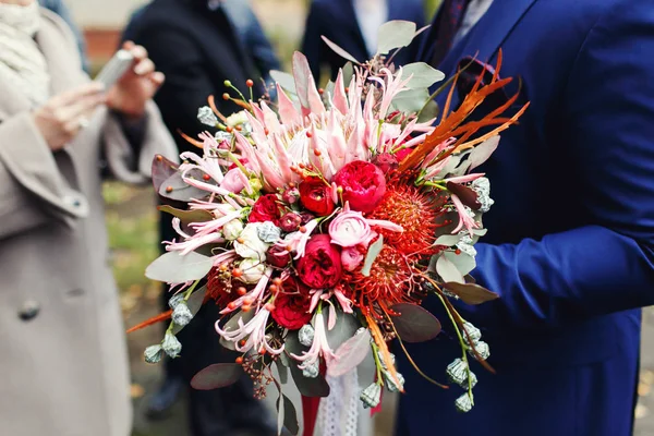 Жених держит потрясающий красный букет из осенних цветов — стоковое фото