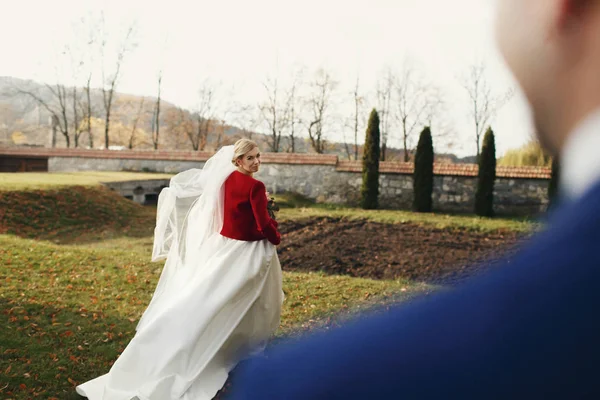 Sposa guarda uno sposo sopra la spalla vestito con una giacca rossa — Foto Stock