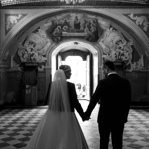 Noiva e noivo saem da igreja segurando suas mãos toget — Fotografia de Stock