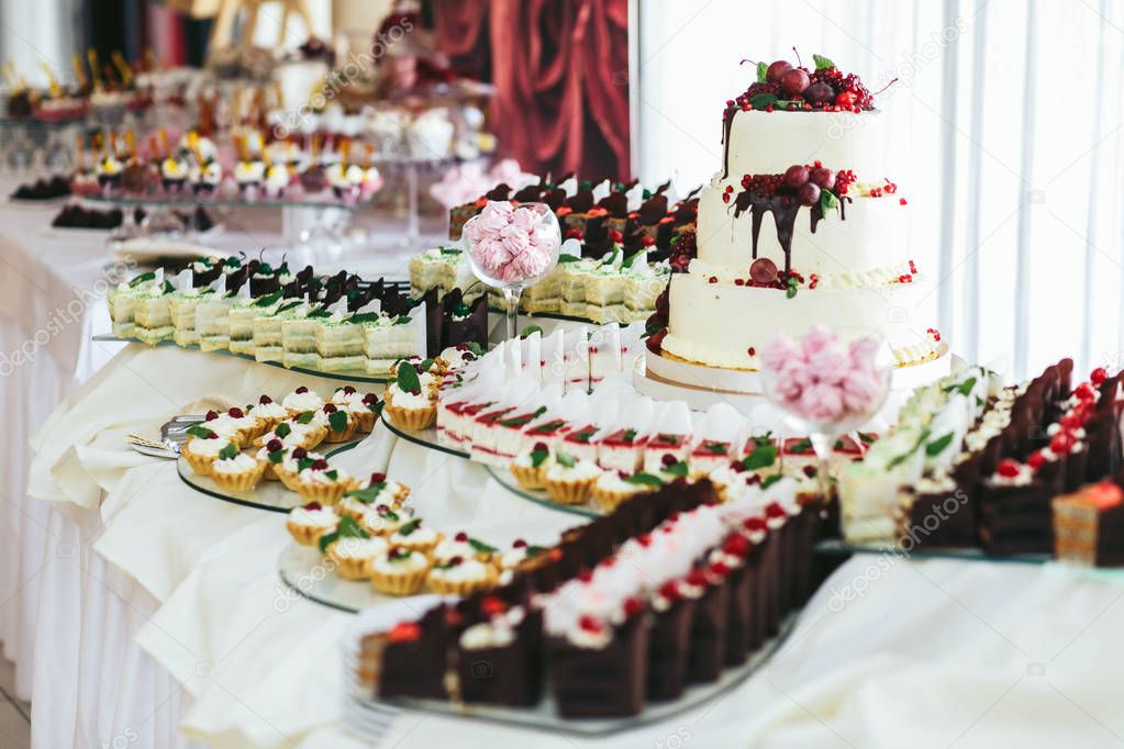 Wedding cake and other baked sweets stand on a dinner buffet 