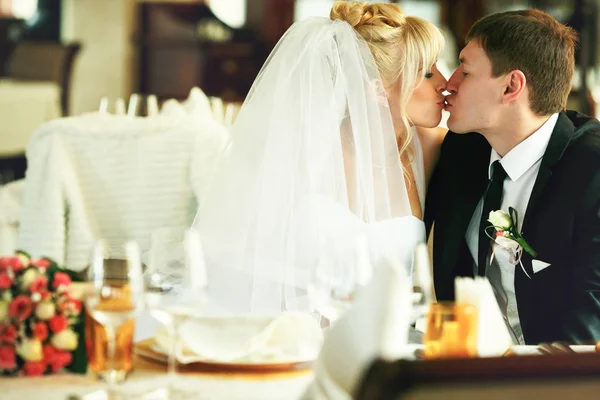 Menyasszony és a vőlegény csók, ül az üres esküvői asztal — Stock Fotó
