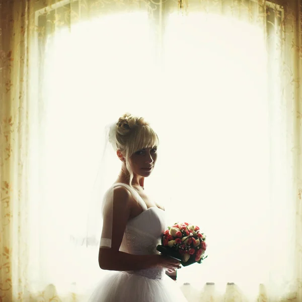 Невеста выглядит заботливо стоя в дневной свет распространяется через — стоковое фото