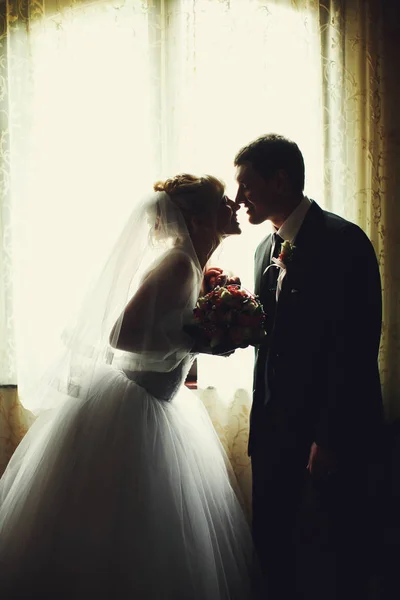 A noiva consegue ao nariz de gromm que está atrás de uma janela — Fotografia de Stock