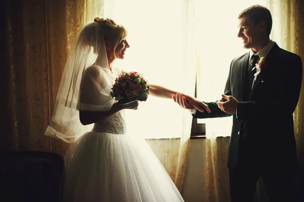 Noivo segura a mão da noiva ternamente em pé na frente de um wi — Fotografia de Stock
