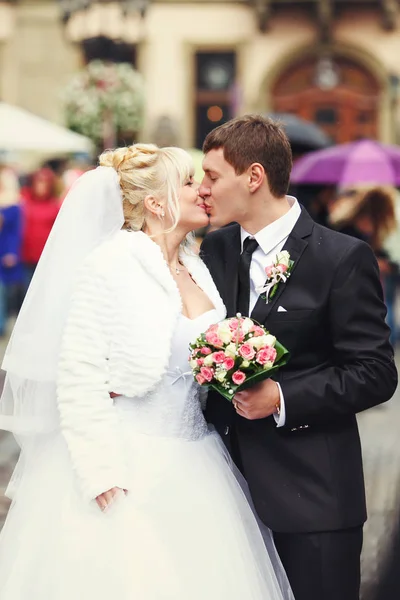 Γαμπρός φιλιά μια νύφη που στέκεται σε ένα βροχερό καιρό κάπου στο th — Φωτογραφία Αρχείου