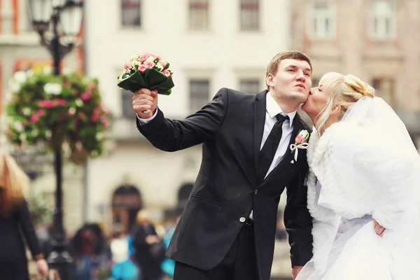 Bride kisses groom's cheek while he holds her bouquet — Stock Photo, Image