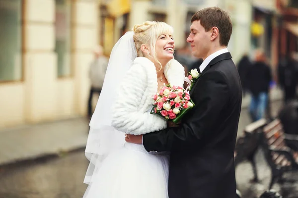 Noiva sorri sendo abraçada por um noivo na rua — Fotografia de Stock