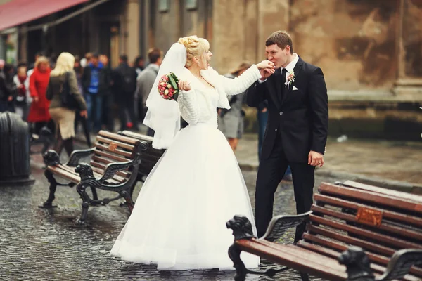 Bräutigam küsst Braut die Hand, die zwischen Bänken auf einer alten Straße steht — Stockfoto