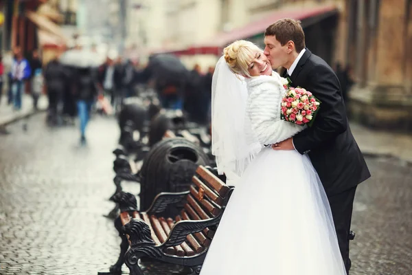 Sposo piega sposa sopra in piedi dietro le panchine sulla strada — Foto Stock