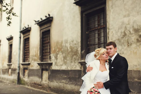 Os recém-casados ficam pensativos atrás de um edifício antigo. — Fotografia de Stock