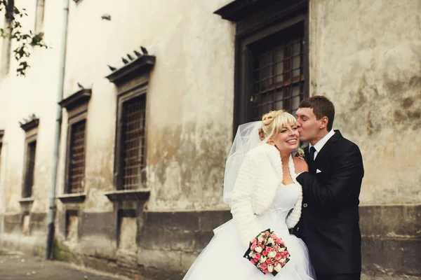Bräutigam küsst charmante Braut, die zärtlich hinter einem alten Gebäude steht — Stockfoto