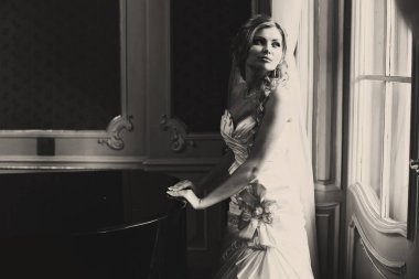 Gelin bir piyano arkasında ışığında duruyor 