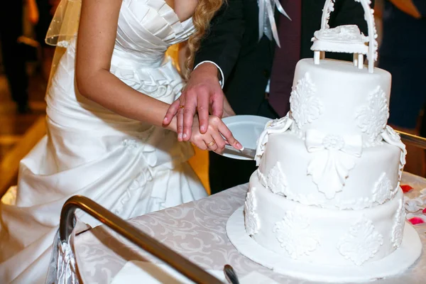 Brudgummen har brudens hand ömt medan hon klipper en bröllopstårta — Stockfoto