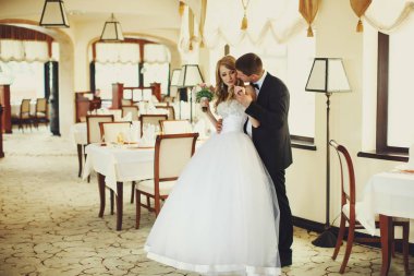 Damat gelin elini şefkatle ayakta tutan arkasından sarılarak 