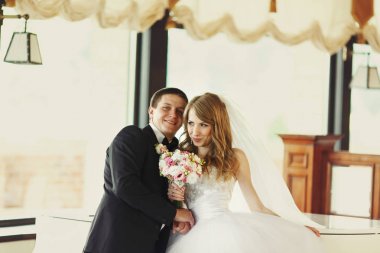 Bir salonda bir piyanoda yaslanmış iken düğün çift gülümsüyor 