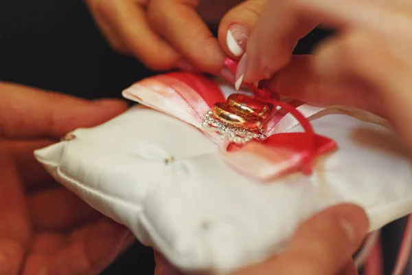 Zlaté snubní prsteny leží na bílém polštáři s červenou stužkou — Stock fotografie