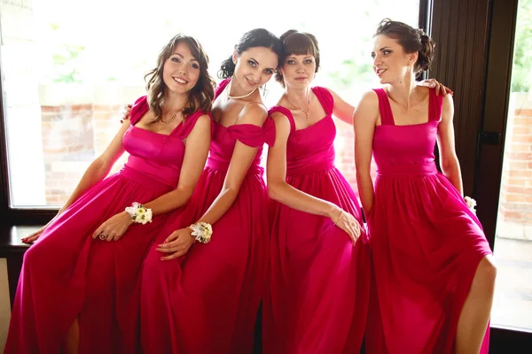 Mooie bruidsmeisjes in roze jurken zitten achter een groot raam — Stockfoto
