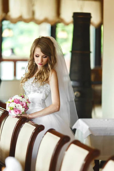 Étonnante mariée regarde vers le bas posant derrière une chaise dans un restaurant — Photo