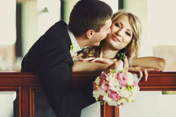 Groom embrasse la joue de la mariée pendant qu'elle se penche sur une main courante en bois — Photo