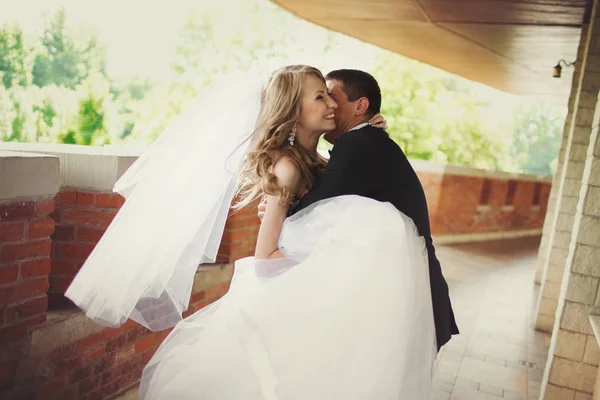 Groom abraça uma noiva sorridente em pé na varanda de tijolo — Fotografia de Stock