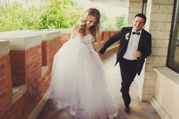Невеста выглядит застенчивой бегая с женихом вдоль кирпичного балкона — стоковое фото