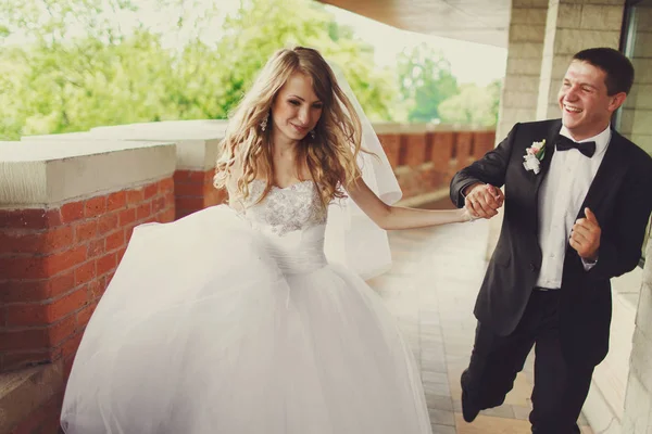 Bräutigam sieht glücklich aus, als er mit einer Braut über den gemauerten Balkon läuft — Stockfoto