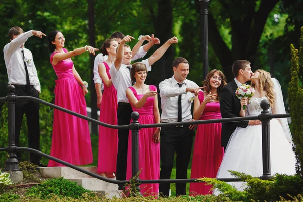 Bridesmaids and groomsmen stare at a kissing wedding couple — Stock Photo, Image