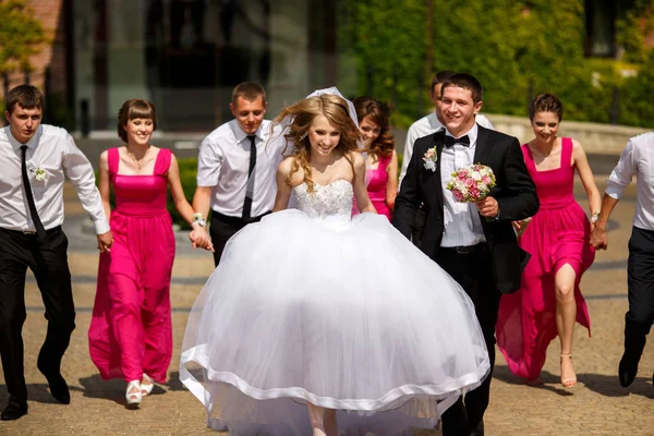 Bruden och brudgummen promenera i parken följs av sina vänner — Stockfoto