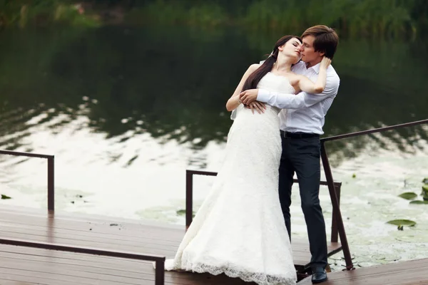 Наречена нахиляється над нареченим, цілуючи його на річковому причалі — стокове фото