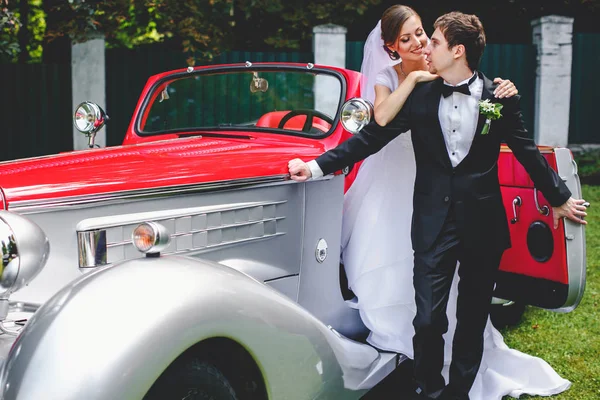 La mariée s'appuie sur un marié debout sur le seuil d'une voiture d'époque — Photo