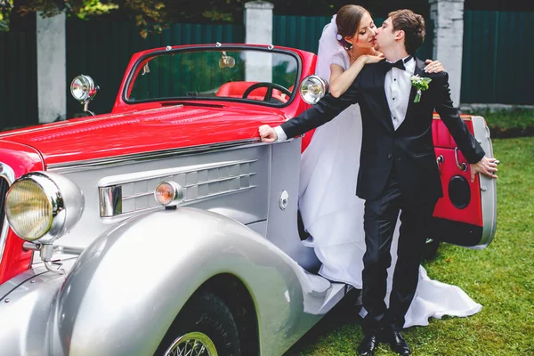 Noiva e noivo beijo de pé em um carro vintage aberto — Fotografia de Stock