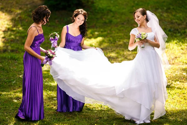 Dama de honra espalhar vestido de noiva de pé na grama no parque — Fotografia de Stock