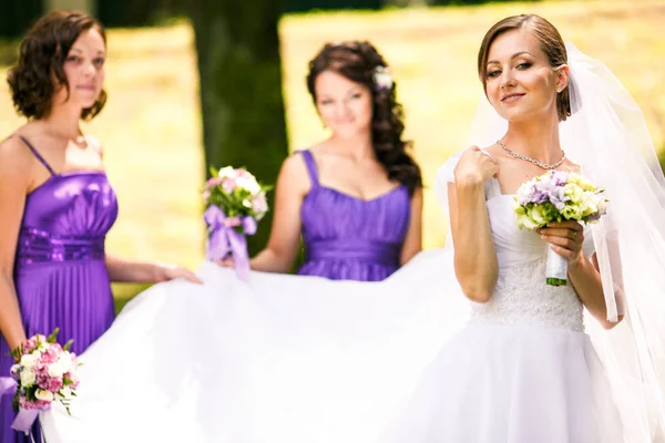Noiva parece orgulhosa enquanto damas de honra segurar seu vestido — Fotografia de Stock