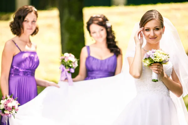 Noiva parece bonita em seu vestido enquanto damas de honra ficar no b — Fotografia de Stock