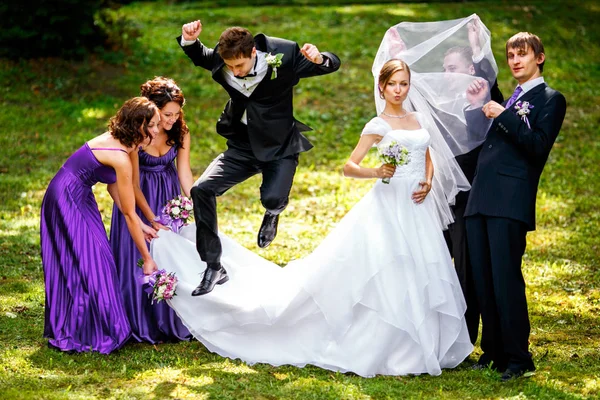 Sposo salta sopra abito della sposa mentre damigelle tenerlo e gro — Foto Stock