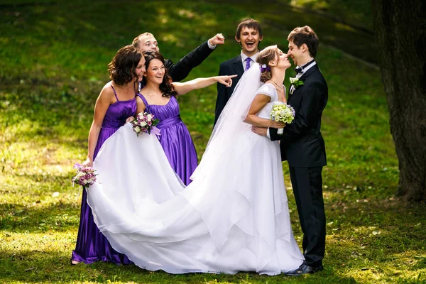 Amigos estendem os dedos aos recém-casados enquanto se beijam — Fotografia de Stock