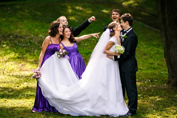 Grimasa přátel, zatímco novomanželé políbil za nimi v parku — Stock fotografie