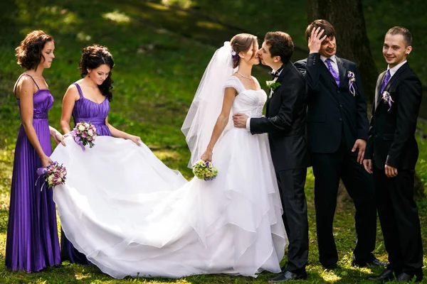 Bräutigam küsst eine Braut, während seine Freunde Grimassen hinter sich lassen — Stockfoto