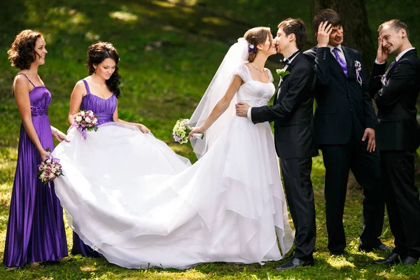 Padrinhos olhar engraçado pé atrás de um beijo casamento casal — Fotografia de Stock