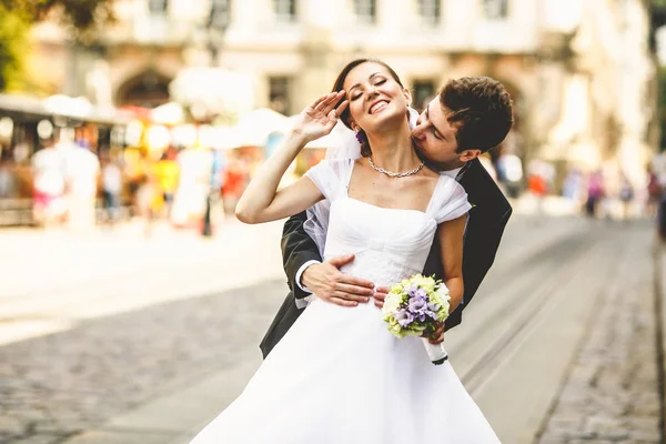 Novio besa un cuello de novia sonriente posando en las calles de ol — Foto de Stock