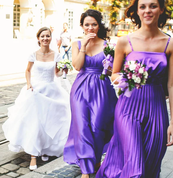 Bride follows bridesmaids walking along an old street — Stock Photo, Image