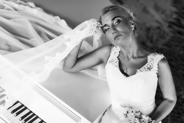 Noiva parece maravilhoso de pé atrás de um piano e segurando-a ele — Fotografia de Stock