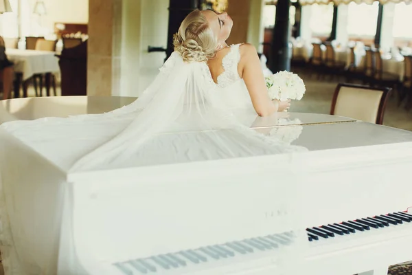 Bruden böjer sig över ett piano och sin slöja sprider sig över den — Stockfoto