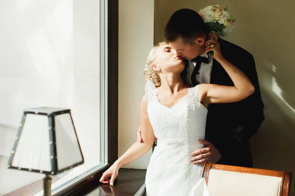 Bride kisses a groom while he hugs her from behind standing in t — Stock Photo, Image