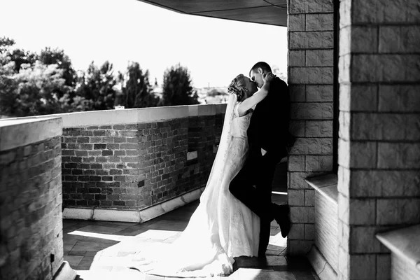 Braut küsst einen Bräutigam, der sich auf dem Balkon an die Wand lehnt — Stockfoto