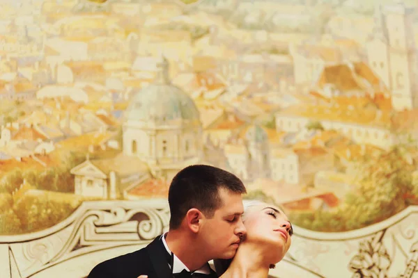 Groom embrasse le cou de la mariée debout derrière un mur avec des peintures — Photo