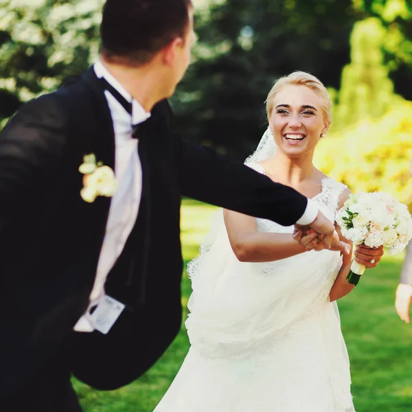 Bräutigam hält Braut die Hand, während sie durch den Park laufen — Stockfoto